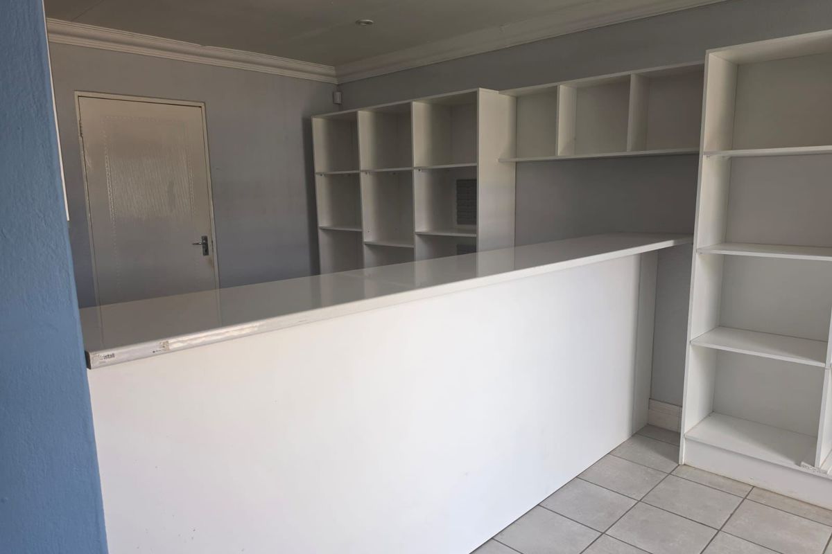 A functional commercial office space featuring a built-in reception counter, extensive integrated shelving, tiled flooring, and recessed lighting.