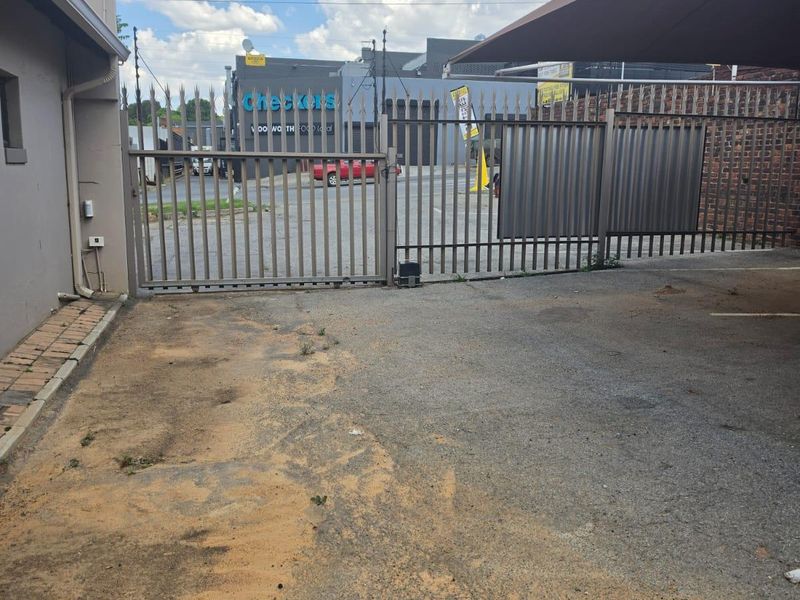 Rear exterior area featuring an asphalt driveway, metal security gate, and shade sail structure, providing access to the commercial property.