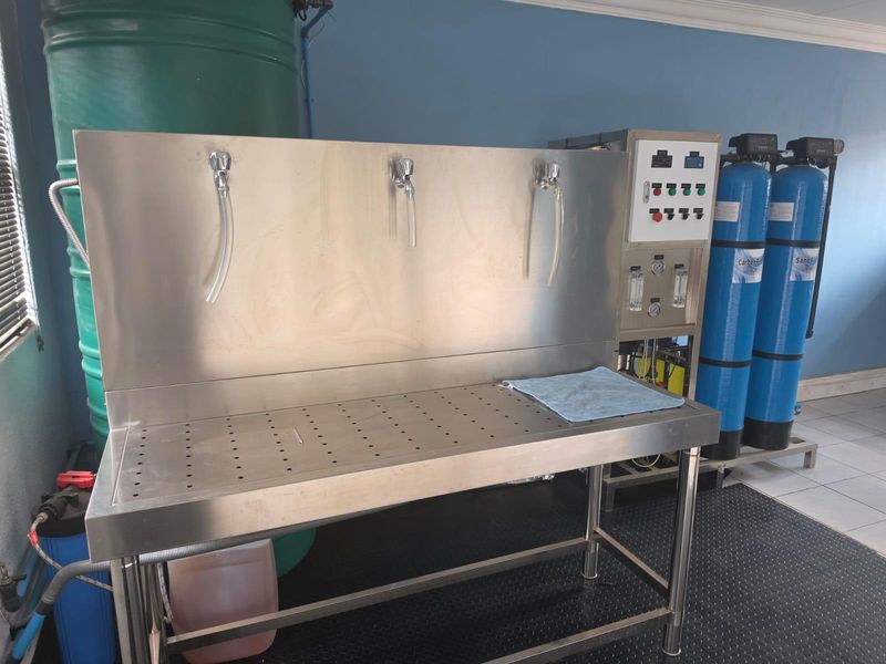A functional utility space featuring a stainless steel workstation, integrated water filtration system, and industrial water tanks, suitable for commercial processing or maintenance tasks.
