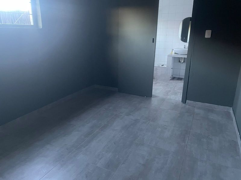 An empty bedroom featuring modern grey floor tiles and a direct view into an adjoining en-suite bathroom with a vanity basin.