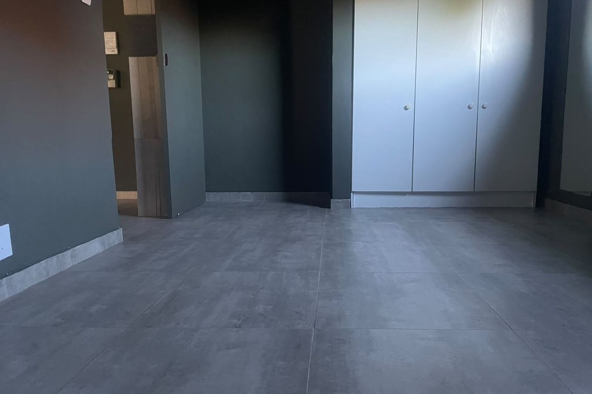 An empty bedroom featuring modern grey floor tiles and built-in white cupboards against dark painted walls.