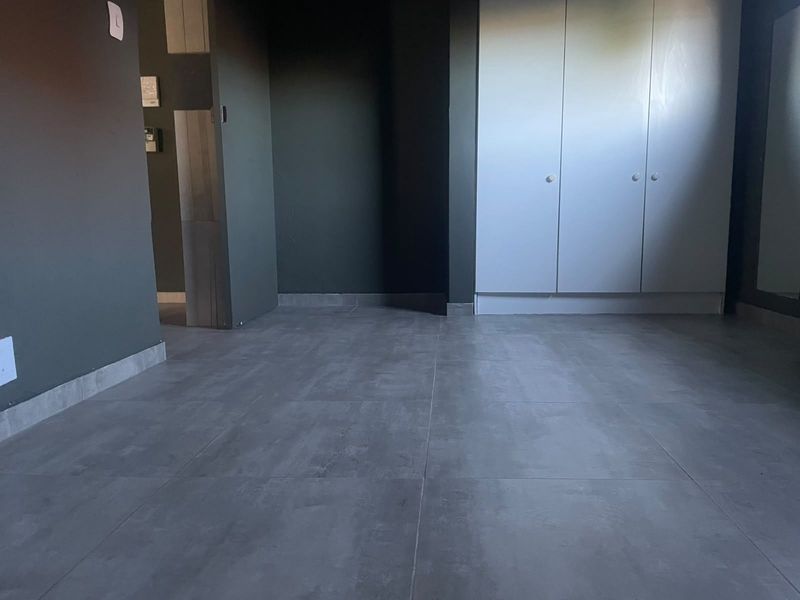An empty bedroom featuring modern grey floor tiles and built-in white cupboards against dark painted walls.