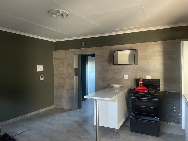 A functional kitchen area featuring a built-in stove, extractor fan, and a breakfast bar with modern tiled splashbacks and flooring.
