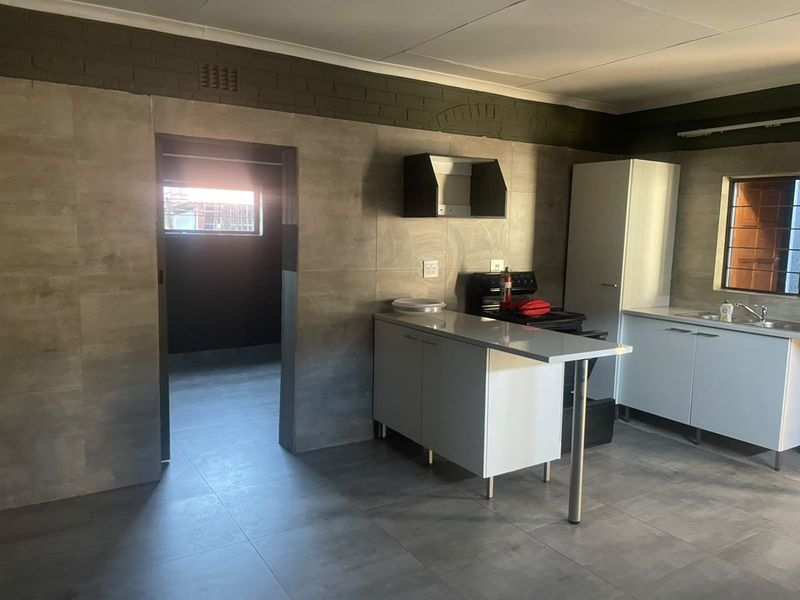 A functional kitchen featuring modern grey wall and floor tiles, built-in cabinetry, a stove, and a sink, with an adjacent utility area.