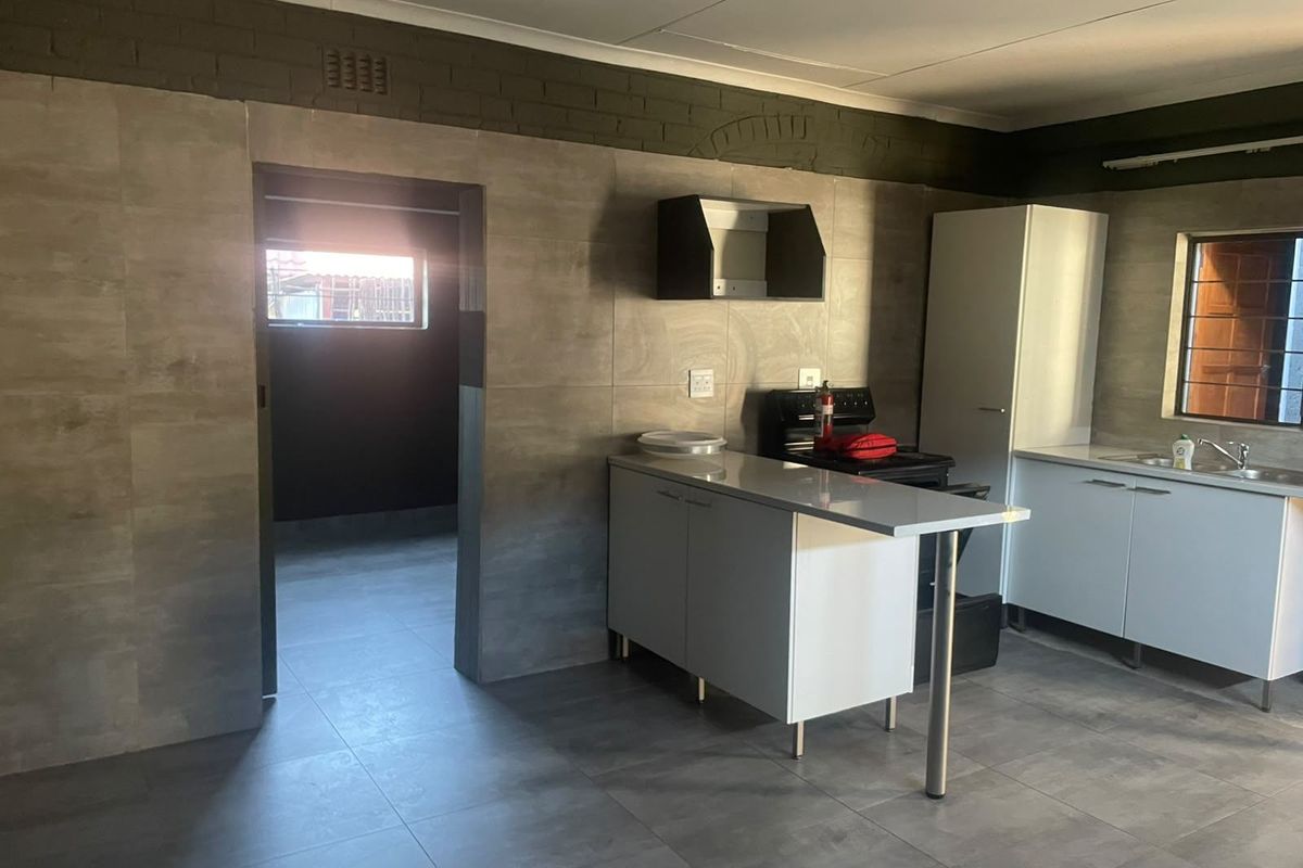 A functional kitchen featuring modern grey wall and floor tiles, built-in cabinetry, a stove, and a sink, with an adjacent utility area.