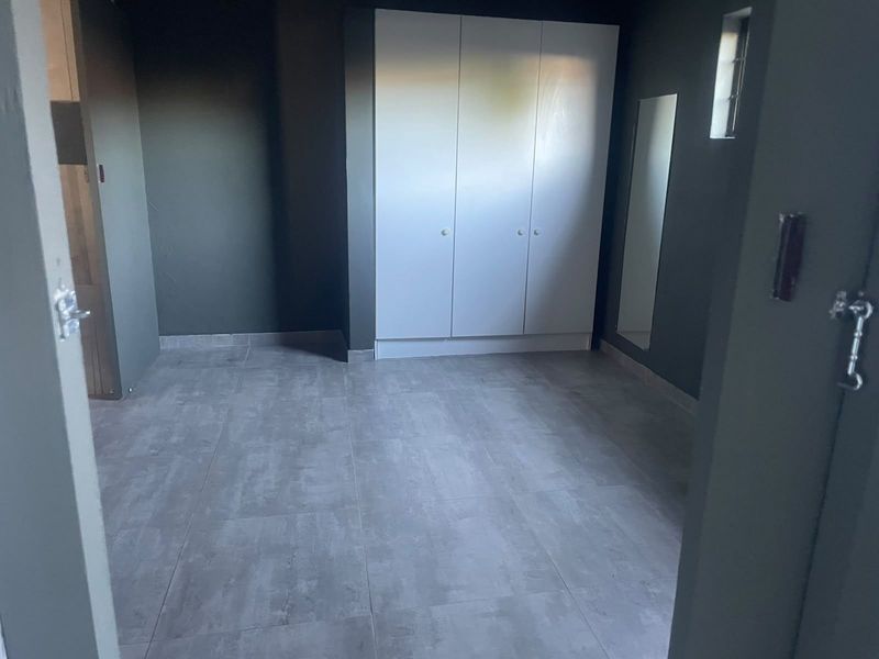 A clean, empty bedroom featuring modern grey tiled flooring, dark painted walls, and built-in white cupboards.