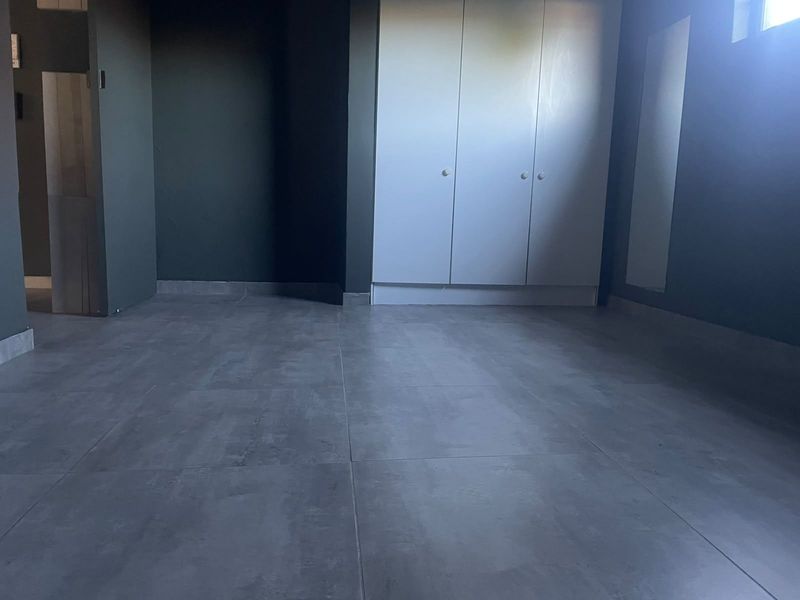 An empty bedroom featuring modern grey tiled flooring and a built-in white wardrobe.