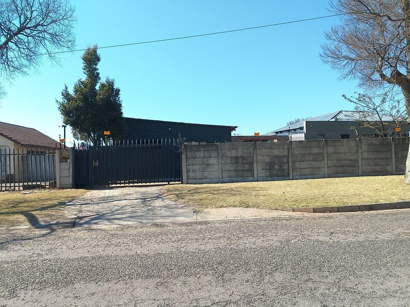 Front exterior view of the property featuring a secure precast concrete boundary wall with razor wire and a metal driveway gate.