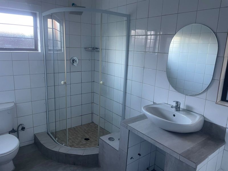 A functional bathroom featuring a corner shower enclosure, a built-in vanity with a basin, and a toilet, finished with white wall tiles.