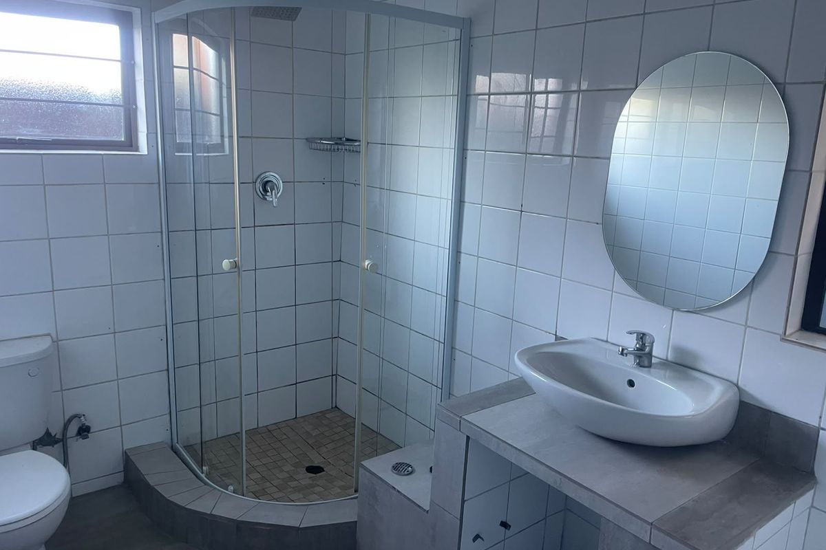 A functional bathroom featuring a corner shower enclosure, a built-in vanity with a basin, and a toilet, finished with white wall tiles.