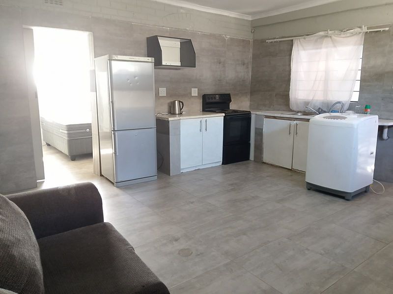 A functional kitchen area featuring tiled flooring, built-in cabinetry, and a freestanding stove, currently requiring cosmetic finishing to the walls.