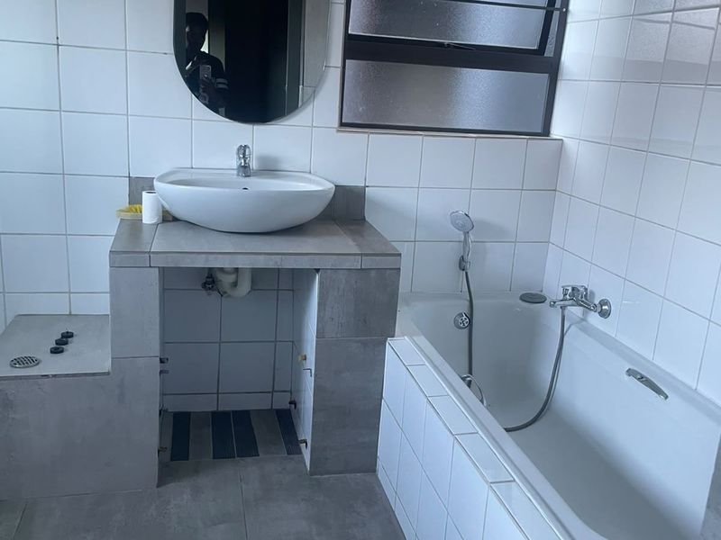 A functional bathroom featuring a tiled bathtub, vessel sink on a tiled vanity, and neutral wall tiling. The vanity base requires finishing.