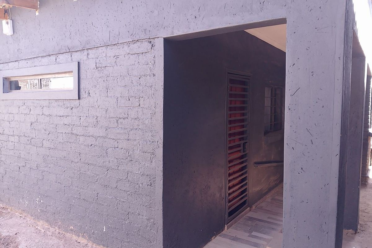 Exterior view of a rear building section featuring a dark painted brick facade, a security gate, and a tiled walkway.