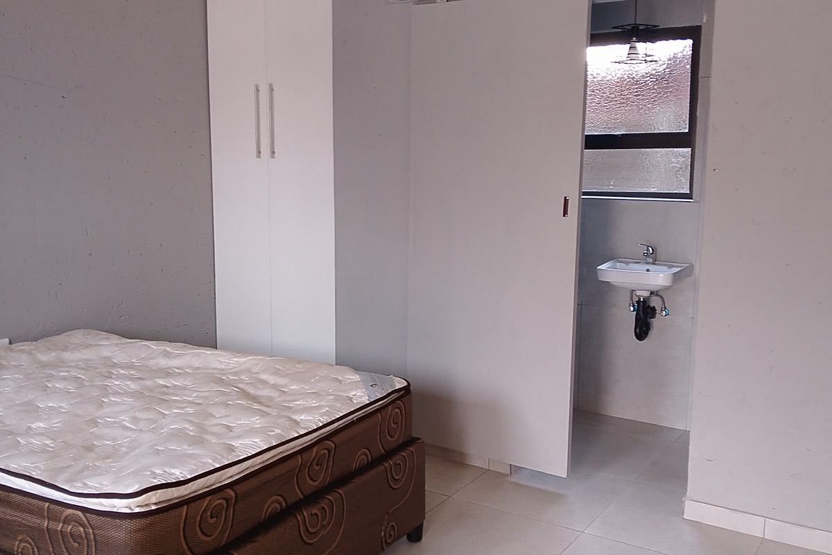 A bedroom featuring tiled flooring, a built-in wardrobe, and a sliding door leading to an en-suite area with a wall-mounted basin.