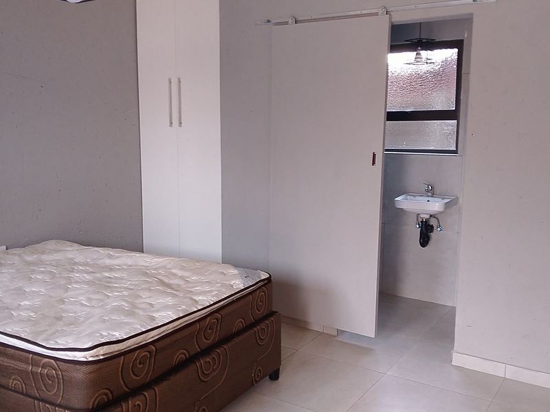 A bedroom featuring tiled flooring, a built-in wardrobe, and a sliding door leading to an en-suite area with a wall-mounted basin.