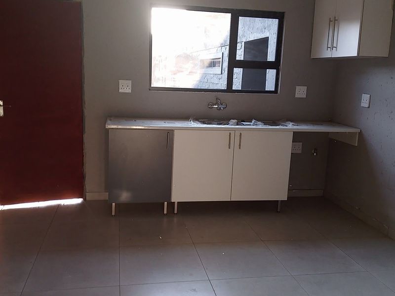 A basic, empty kitchen area featuring tiled floors, simple cabinetry, and a sink, requiring finishing touches to improve its overall aesthetic and functionality.
