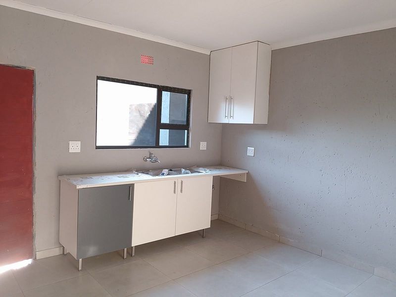 A compact, empty kitchen area featuring basic cabinetry, a stainless steel sink, and tiled flooring, ready for personalization.