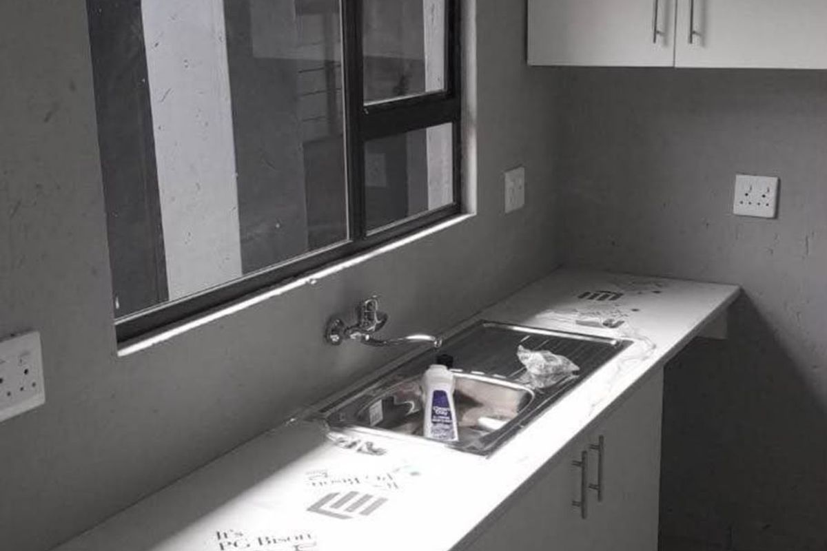 A compact kitchen area featuring modern white cabinetry, a stainless steel sink, and a laminate countertop, currently in an unfinished state.