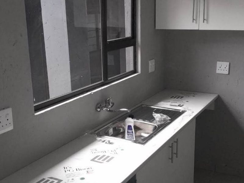A compact kitchen area featuring modern white cabinetry, a stainless steel sink, and a laminate countertop, currently in an unfinished state.