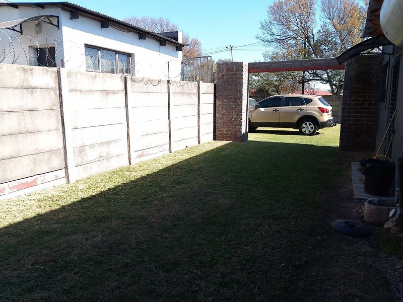 A rear garden area featuring a precast concrete boundary wall with security razor wire and a brick pillar entrance.