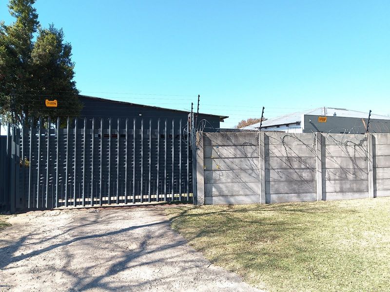Front exterior view featuring a steel security gate, precast concrete boundary wall, and integrated electric fencing with razor wire for enhanced property security.