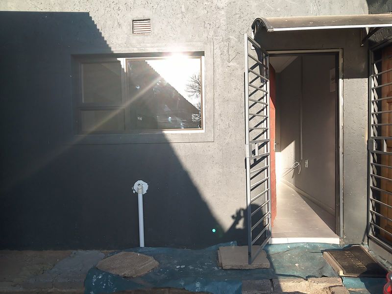 Rear exterior view of the property featuring a security gate, awning, and external wall finishes with visible plumbing and ventilation.