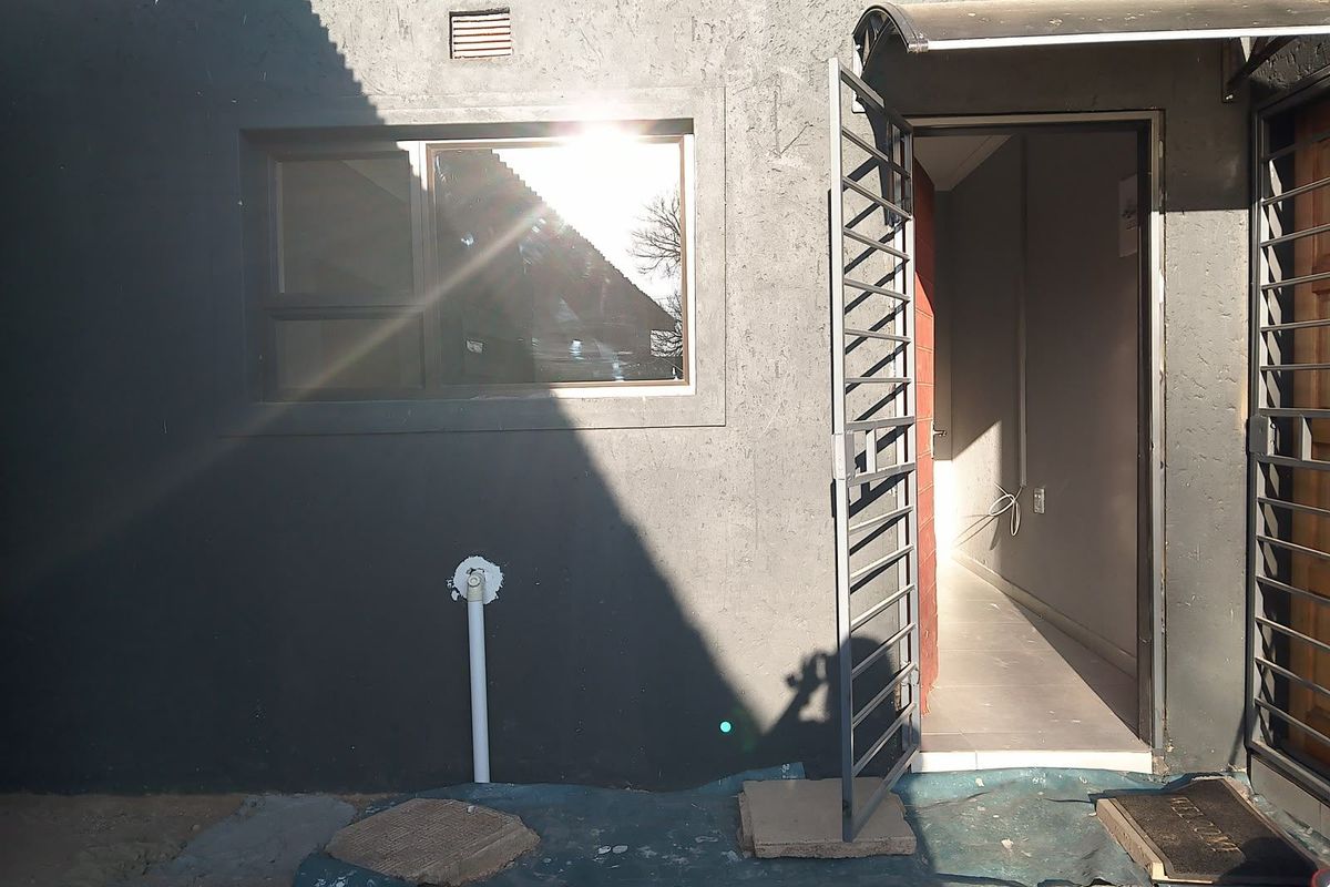 Rear exterior view of the property featuring a security gate, awning, and external wall finishes with visible plumbing and ventilation.