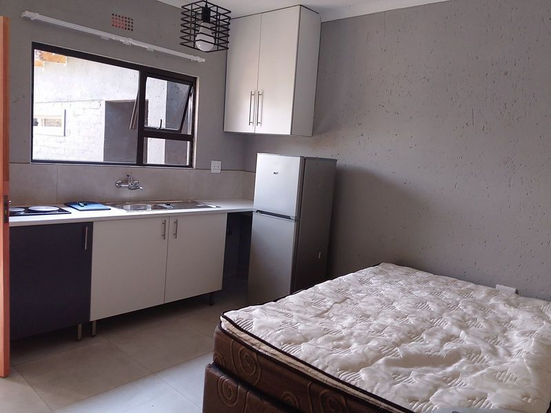 A compact open-plan studio space featuring a modern kitchenette with built-in cabinetry, stainless steel sink, and tiled flooring.