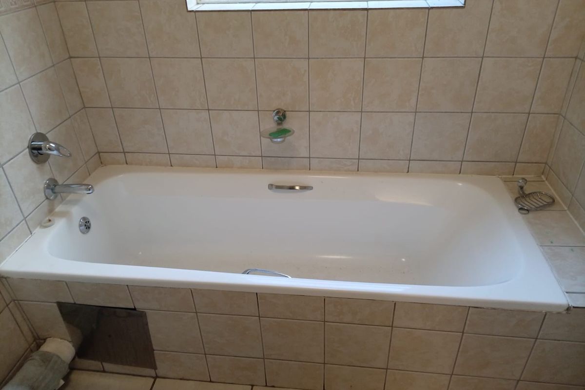 A functional bathroom featuring a built-in bathtub with chrome fixtures and neutral ceramic wall and floor tiling.