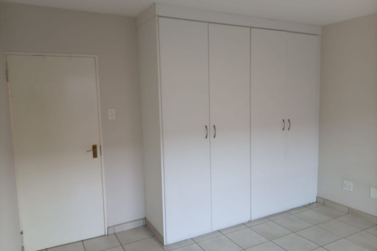 A clean, empty bedroom featuring neutral tiled flooring and ample built-in cupboard storage space.