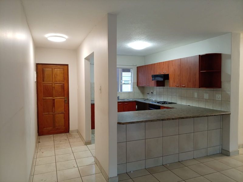 Open plan kitchen area featuring built-in cabinetry, laminate countertops, tiled backsplash, and integrated hob, adjacent to a tiled hallway with a timber entrance door.