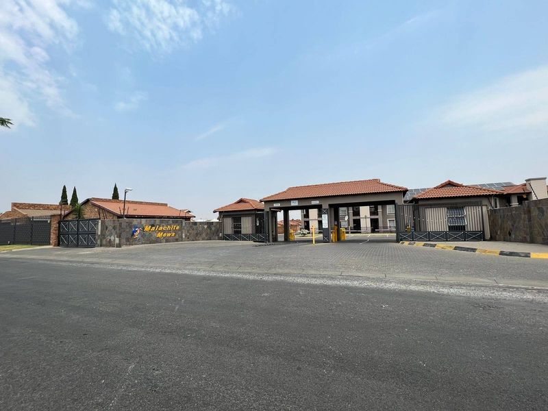 The entrance to Malachite Mews apartment complex, featuring a secure gated access point, paved driveway, and well-maintained perimeter wall with stone cladding.