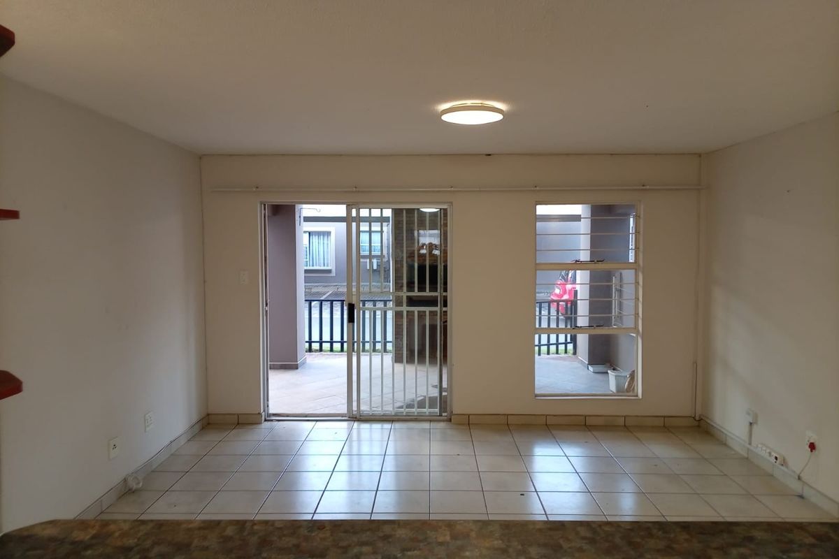 An empty living area featuring tiled flooring, a sliding glass door with security gate, and access to an outdoor patio area.
