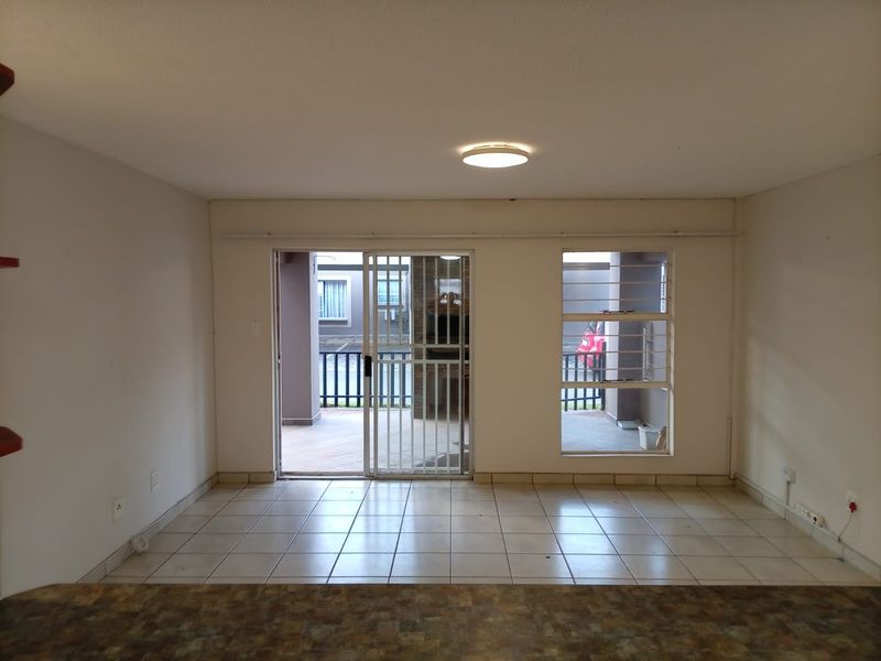 An empty living area featuring tiled flooring, a sliding glass door with security gate, and access to an outdoor patio area.
