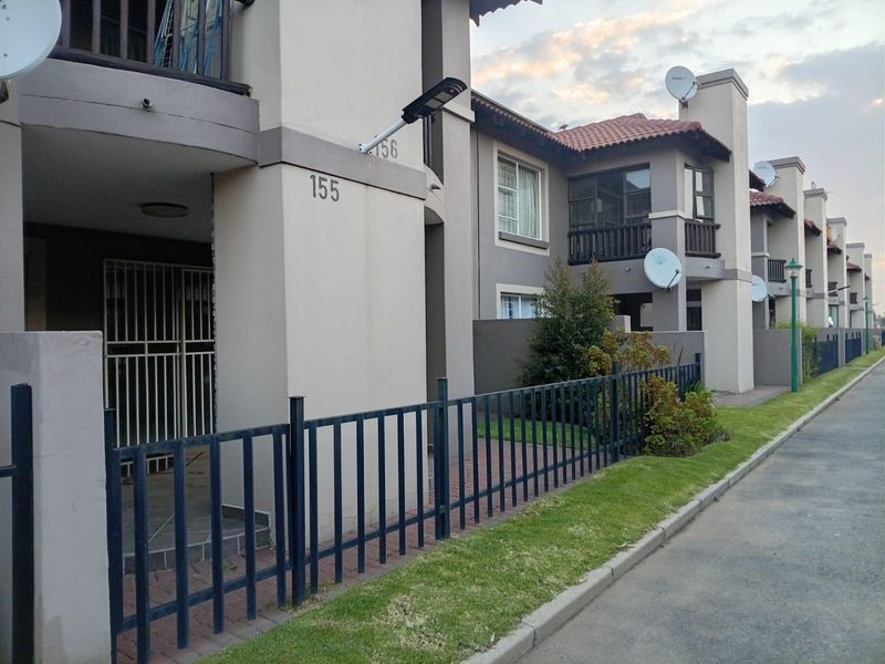 Exterior view of a multi-unit apartment complex featuring paved walkways, metal perimeter fencing, and private ground-floor patio areas with security gates.
