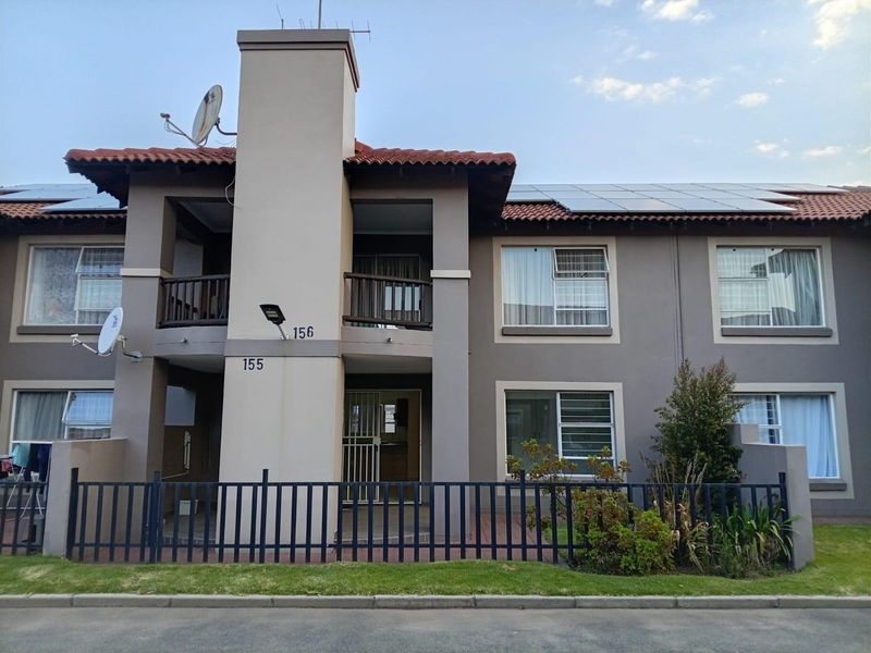 Front elevation of a two-story apartment complex featuring terracotta roof tiles, solar panels, and private balcony access with secure metal fencing.