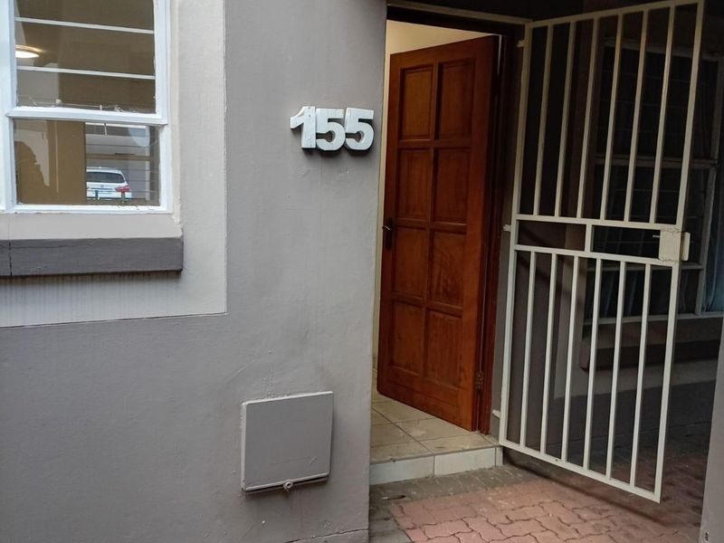 Entrance area of the apartment featuring a security gate, timber door, and paved walkway.