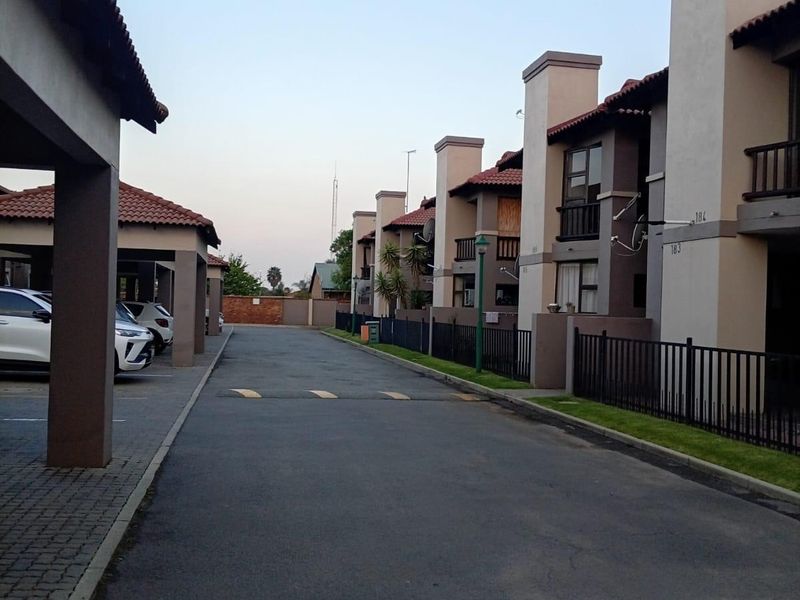 A view of the apartment complex driveway featuring covered parking bays, paved access roads, and multi-story residential units with balconies.