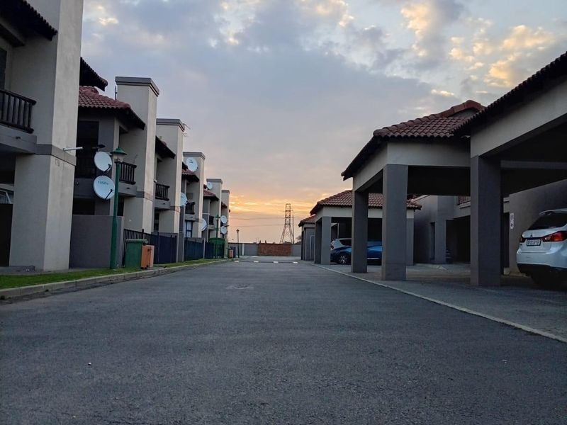 A view of the apartment complex driveway featuring covered parking bays and residential building facades under a sunset sky.