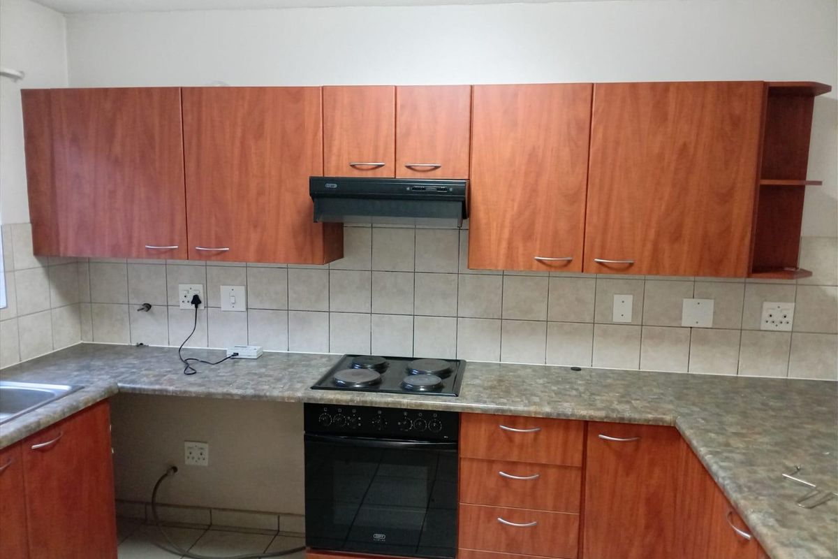 A functional kitchen featuring wood-look laminate cabinetry, a tiled backsplash, built-in oven with hob, and durable countertop surfaces.