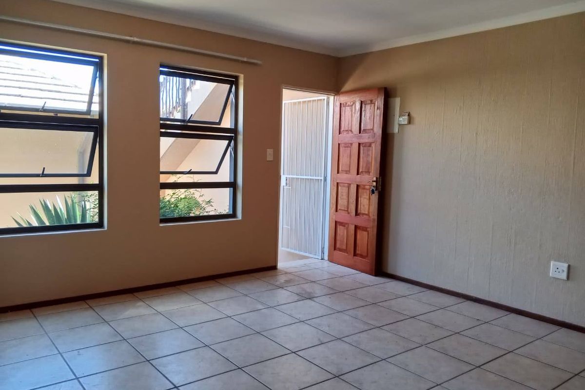 An empty living room featuring tiled flooring, aluminium windows, and a timber door leading to an exterior area.