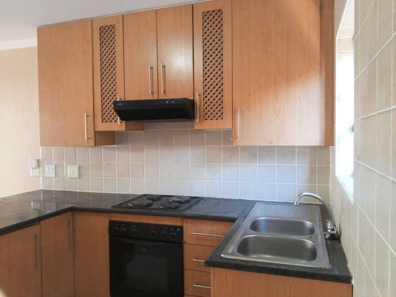 A functional kitchen featuring light wood cabinetry, granite countertops, a built-in oven with hob, and a double bowl stainless steel sink with tiled splashback.