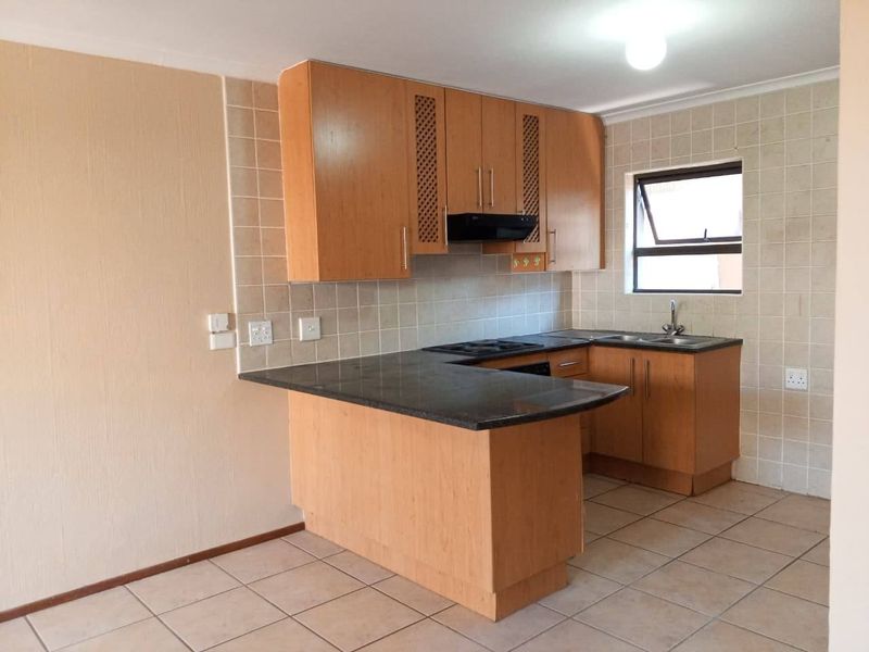 A functional kitchen featuring wooden cabinetry, granite countertops, a built-in hob with extractor fan, and tiled finishes throughout.