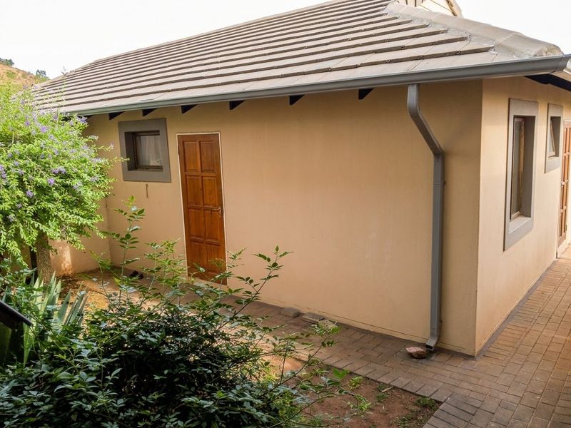 Rear exterior view of the townhouse featuring a tiled roof, paved walkway, and access door with established garden surroundings.