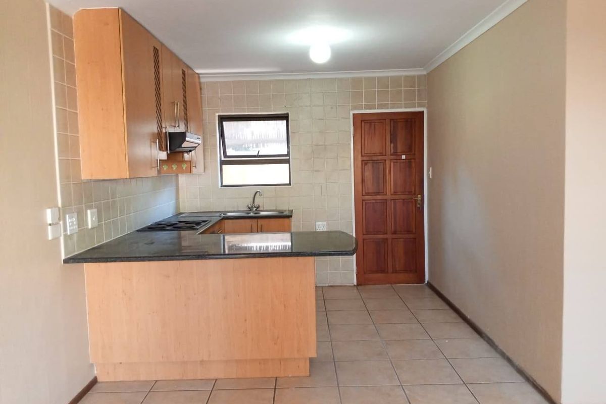 A functional kitchen featuring laminate cabinetry, granite countertops, a built-in hob with extractor, and tiled flooring, offering a clean and practical workspace.