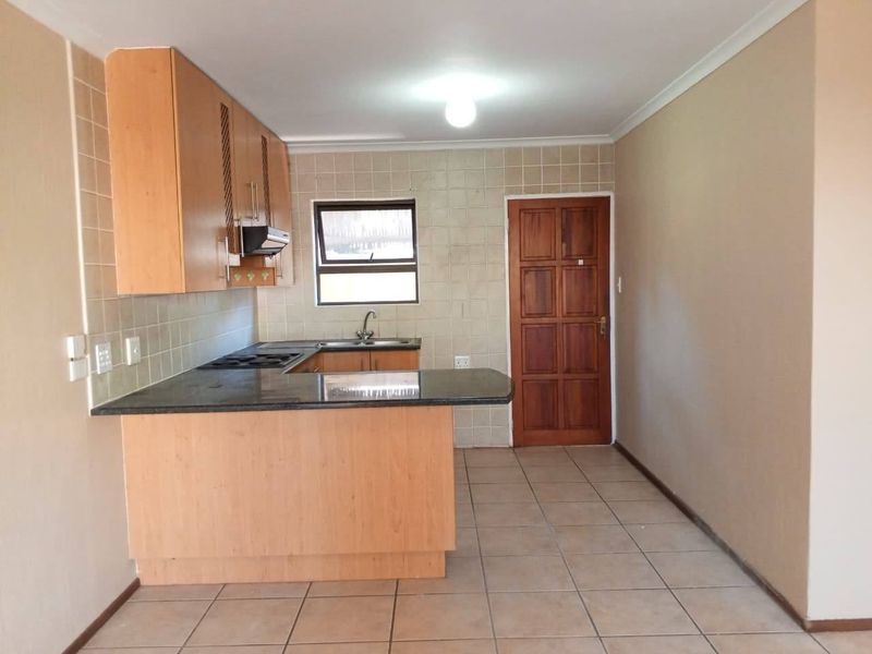 A functional kitchen featuring laminate cabinetry, granite countertops, a built-in hob with extractor, and tiled flooring, offering a clean and practical workspace.