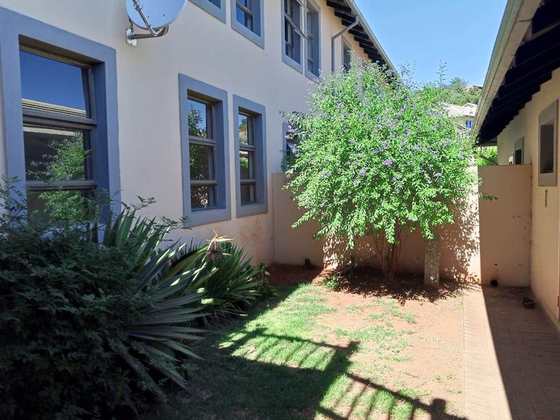 A side garden area featuring a paved walkway, boundary wall, and established landscaping alongside the townhouse exterior.
