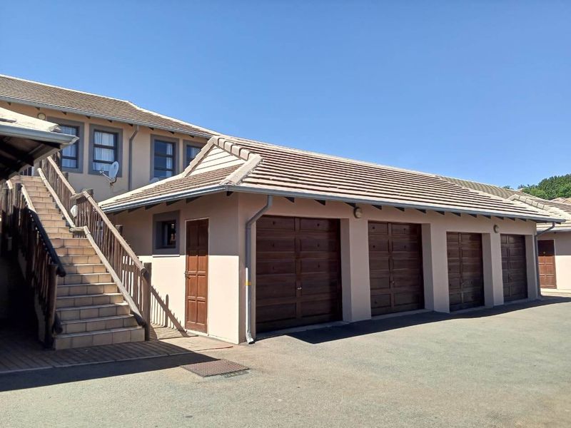 Exterior view of a townhouse complex featuring a row of garages with wooden doors and an external staircase leading to the upper level.