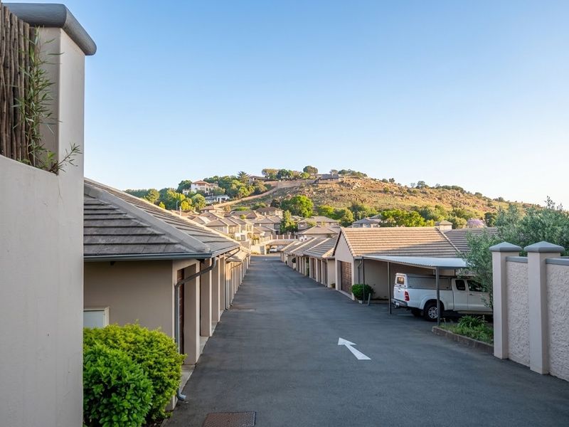 A view down the paved driveway of a residential townhouse complex, featuring rows of garages and carports with a scenic hillside backdrop.