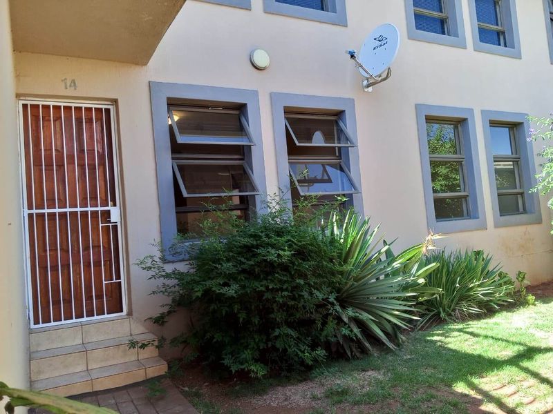 Front entrance of the townhouse featuring a security gate, tiled steps, and top-hung windows with a small garden area.